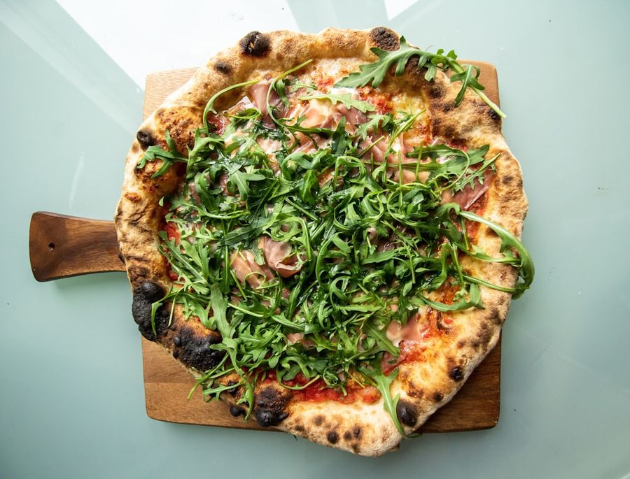 Pizza speciale guarnita con rucola fresca e salumi su tagliere di legno