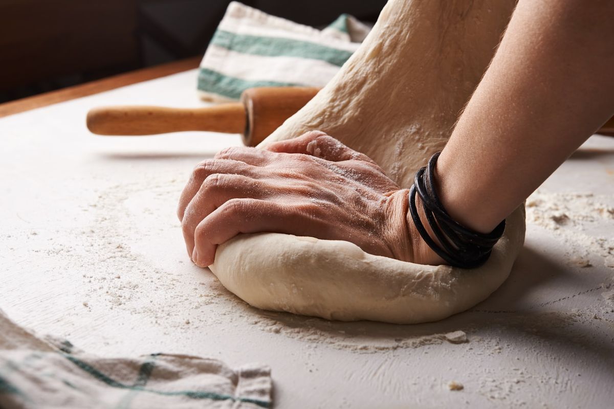Mani che lavorano l'impasto della pizza sul piano infarinato